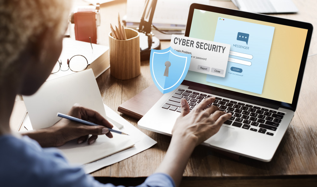 Woman working on laptop with holographic image of shield with lock showing concepts of cybersecurity