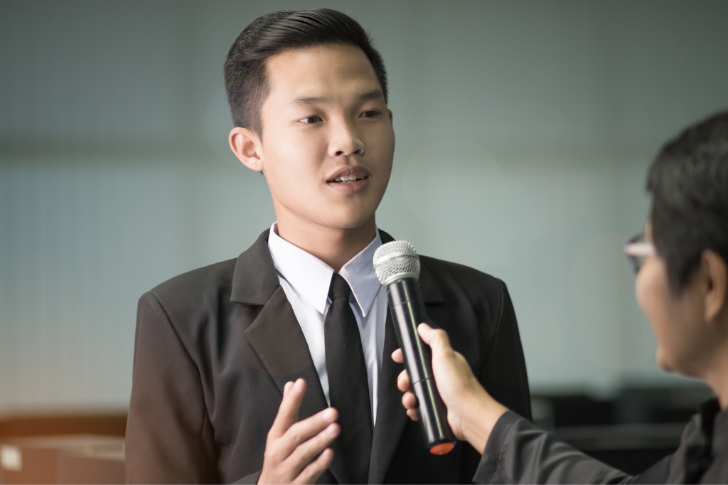 A businessman answering questions from a female reporter holding a microphone