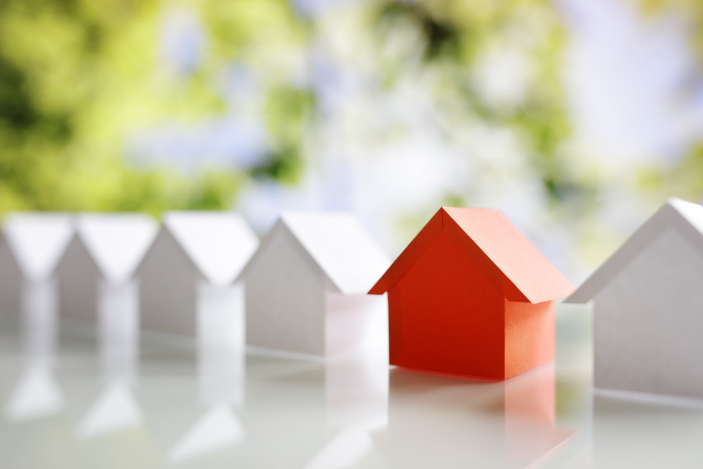 red miniature house in the middle of white ones representing choosing a property