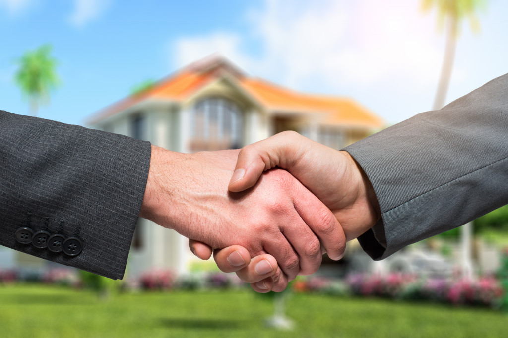 two business people shaking hands in front of a house
